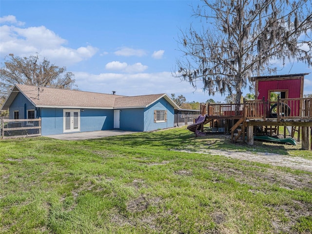 rear view of property featuring a yard, french doors, fence, and stucco siding