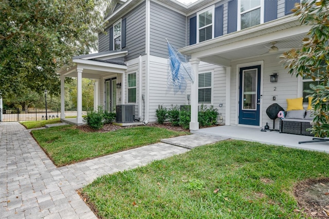 doorway to property featuring a porch, fence, a lawn, and central AC unit