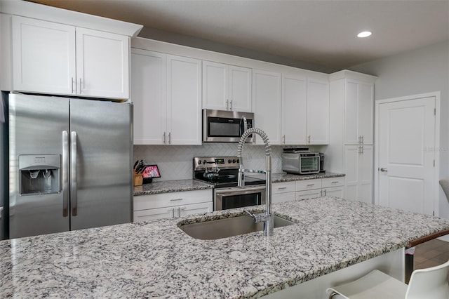 kitchen featuring white cabinetry, appliances with stainless steel finishes, decorative backsplash, and light stone counters