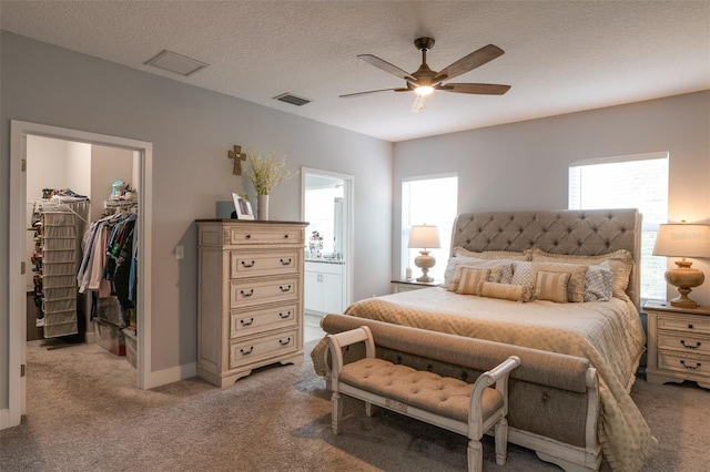 bedroom featuring a textured ceiling, a walk in closet, visible vents, and light colored carpet