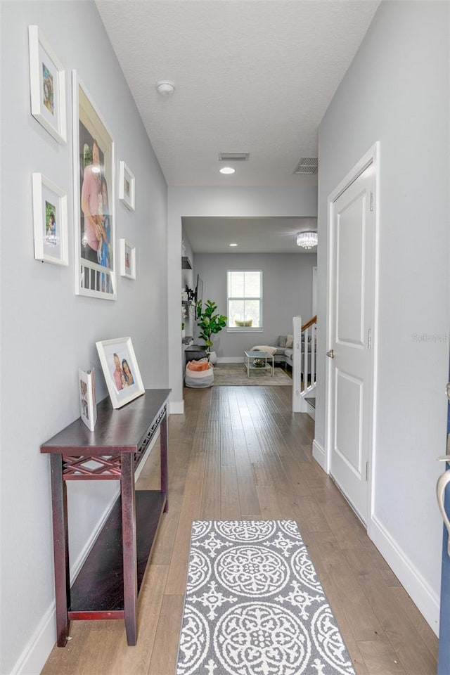 hall featuring stairway, wood-type flooring, visible vents, and baseboards