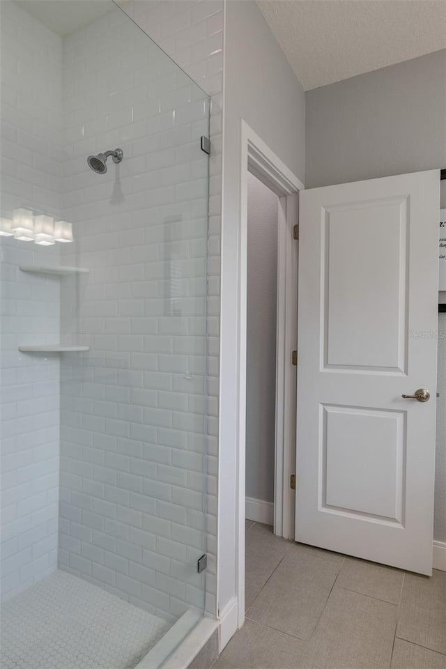 full bathroom featuring a textured ceiling, a stall shower, tile patterned flooring, and baseboards