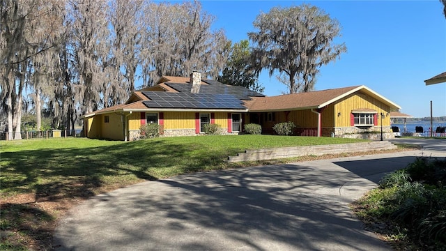 view of front of house with solar panels, fence, concrete driveway, stone siding, and a front lawn