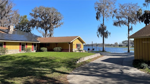 view of front facade featuring concrete driveway, a water view, roof mounted solar panels, and a front lawn