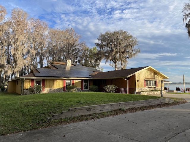 view of front of house with a chimney, concrete driveway, roof mounted solar panels, stone siding, and a front lawn