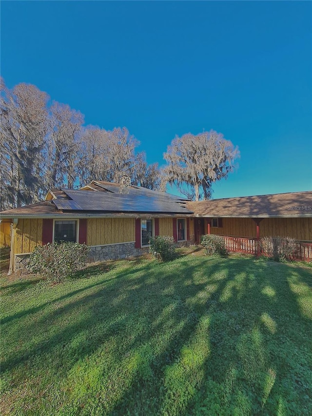 back of house with stone siding and a lawn