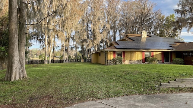 exterior space featuring solar panels, fence, stone siding, a front lawn, and a chimney