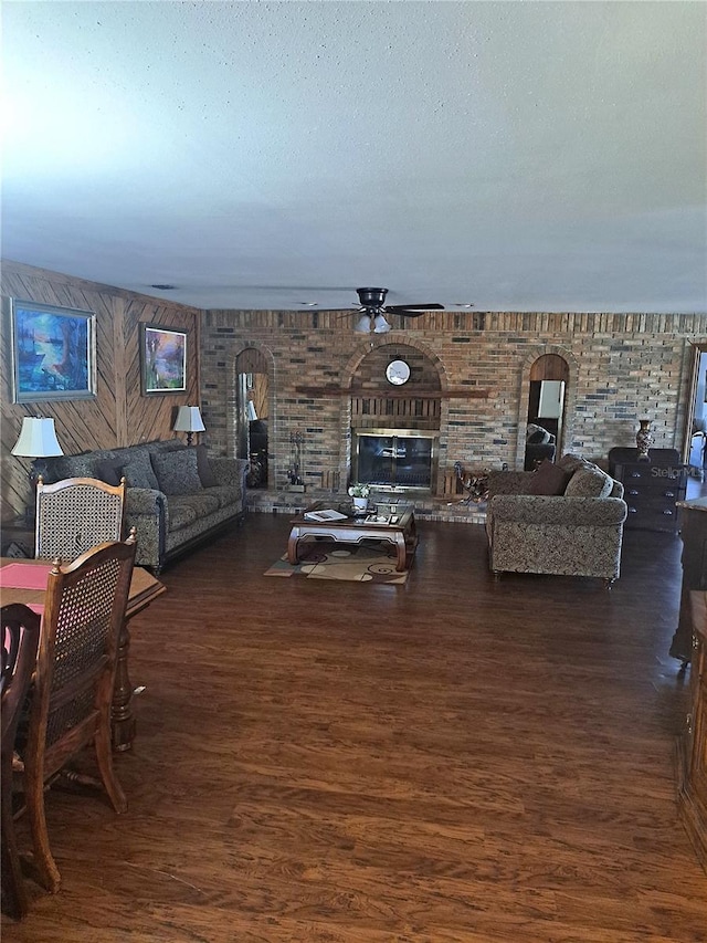 living area with a textured ceiling, ceiling fan, a brick fireplace, and wood finished floors