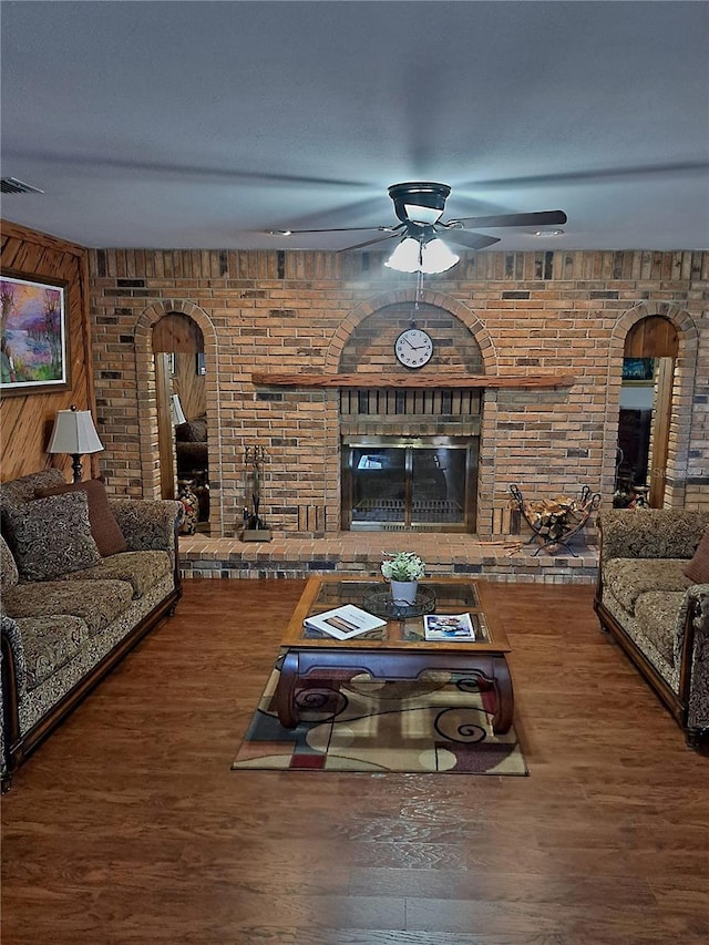 living area with arched walkways, a fireplace, wood finished floors, visible vents, and a ceiling fan