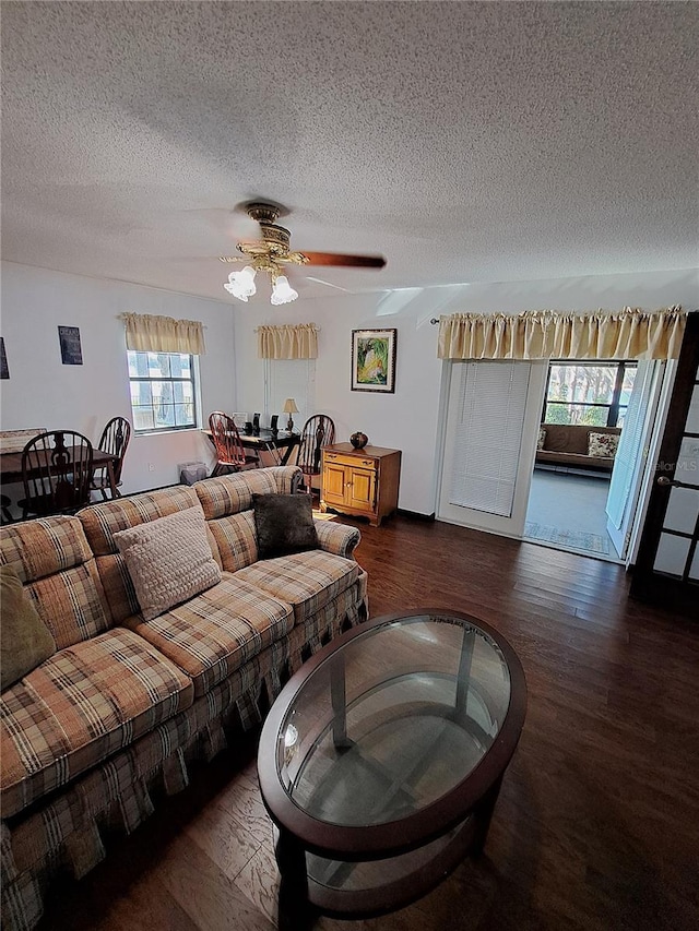 living room featuring dark wood-style flooring, ceiling fan, and a textured ceiling