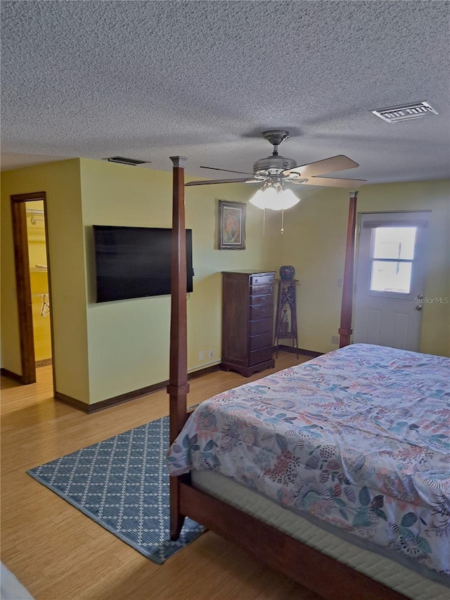 bedroom with a ceiling fan, a textured ceiling, visible vents, and wood finished floors