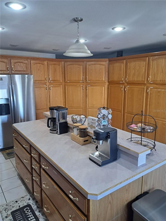 kitchen featuring a center island, light tile patterned floors, light countertops, brown cabinetry, and stainless steel fridge