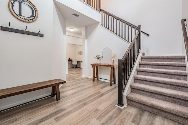 stairway with visible vents, a towering ceiling, baseboards, and wood finished floors