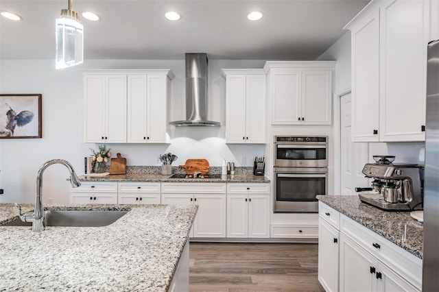 kitchen with white cabinetry, wall chimney exhaust hood, stainless steel double oven, and a sink