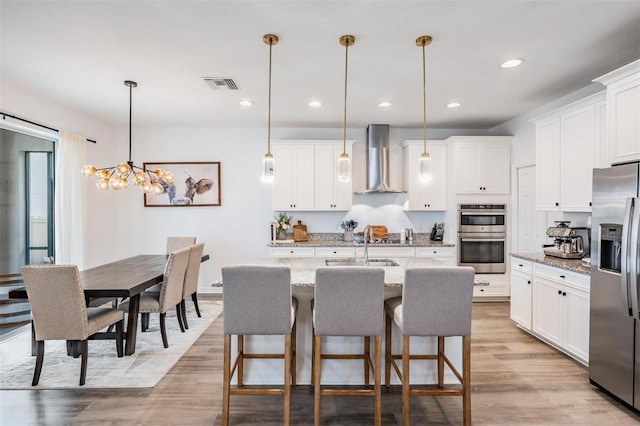 kitchen featuring light wood finished floors, visible vents, wall chimney exhaust hood, stainless steel appliances, and white cabinetry