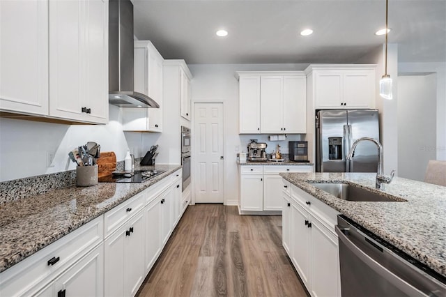 kitchen featuring appliances with stainless steel finishes, wood finished floors, wall chimney range hood, white cabinetry, and a sink