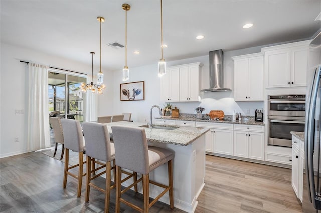 kitchen featuring visible vents, appliances with stainless steel finishes, a sink, wall chimney range hood, and a kitchen breakfast bar