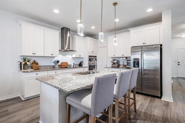 kitchen featuring white cabinetry, appliances with stainless steel finishes, wall chimney exhaust hood, a kitchen bar, and a center island with sink