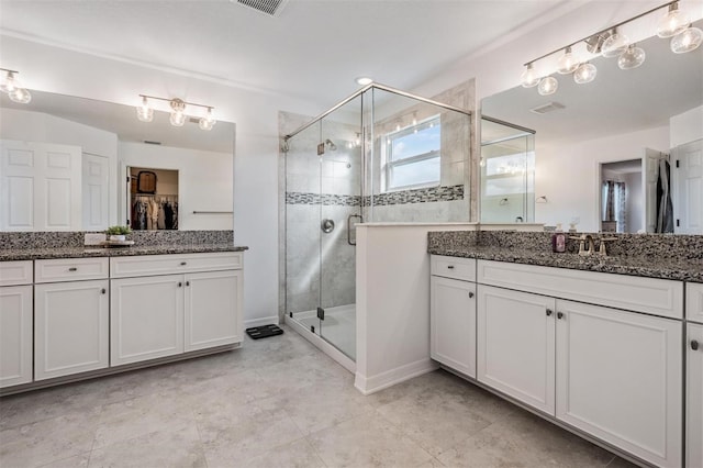 full bathroom featuring a shower stall, a spacious closet, visible vents, and two vanities