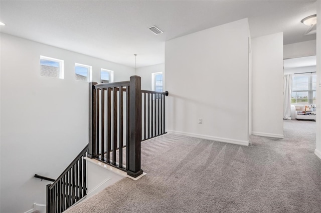 hallway featuring carpet floors, baseboards, visible vents, and an upstairs landing