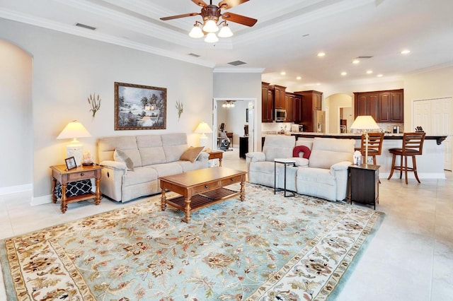 living room with arched walkways, a tray ceiling, crown molding, visible vents, and ceiling fan