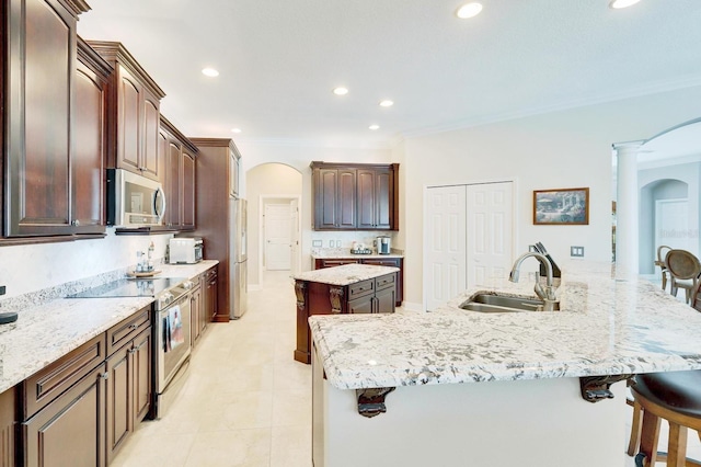 kitchen featuring arched walkways, a spacious island, a kitchen breakfast bar, stainless steel appliances, and a sink