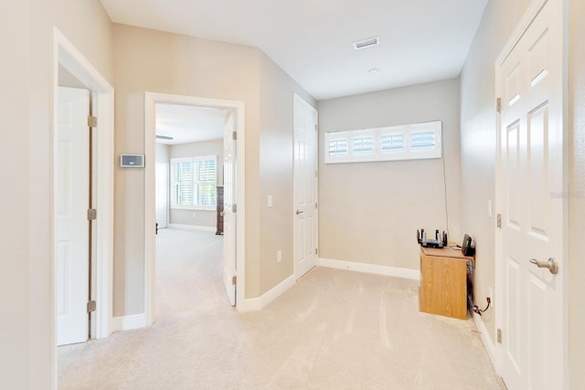 corridor with light carpet, baseboards, and visible vents