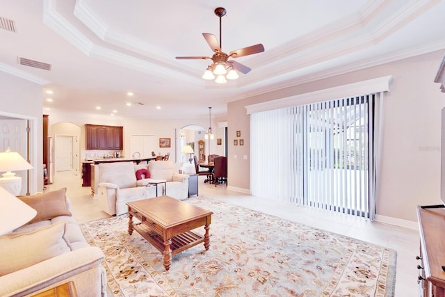 living room featuring light tile patterned floors, arched walkways, a raised ceiling, and ornamental molding