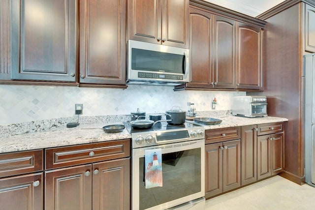 kitchen with dark brown cabinetry, light stone countertops, a toaster, stainless steel appliances, and decorative backsplash