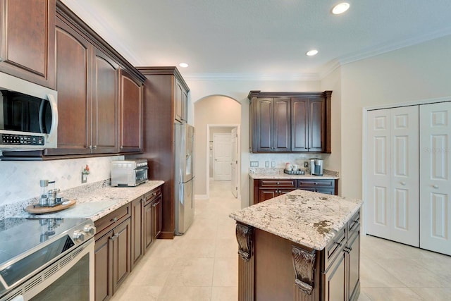 kitchen with light stone counters, arched walkways, crown molding, appliances with stainless steel finishes, and dark brown cabinets