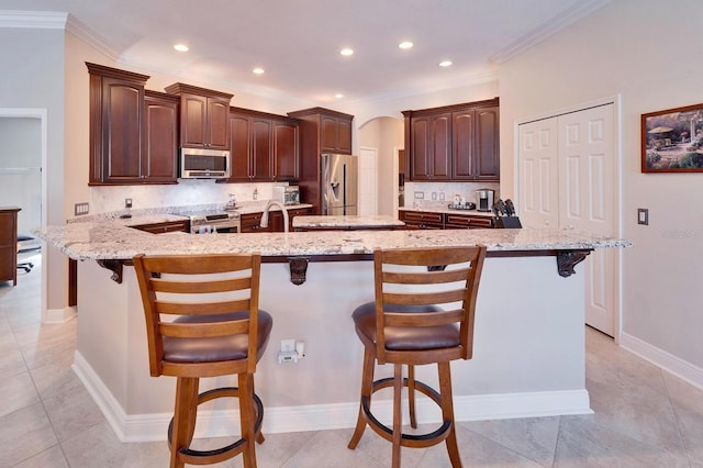 kitchen with appliances with stainless steel finishes, arched walkways, decorative backsplash, and a kitchen bar