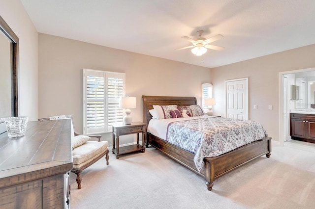 bedroom with baseboards, ceiling fan, ensuite bath, and light colored carpet