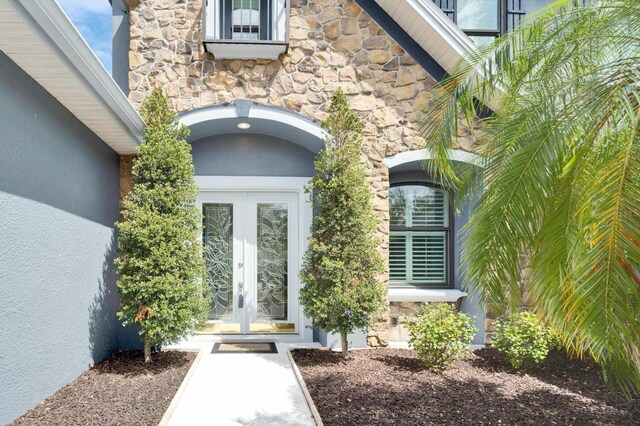 entrance to property with stone siding, french doors, and stucco siding