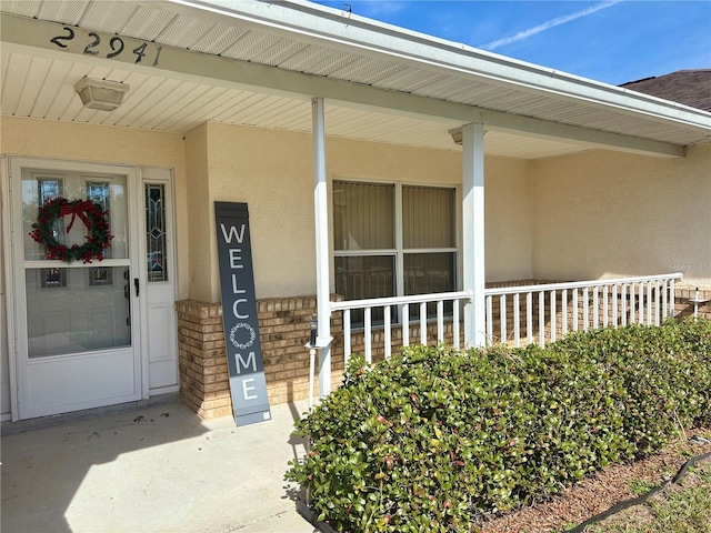 property entrance featuring covered porch, brick siding, and stucco siding