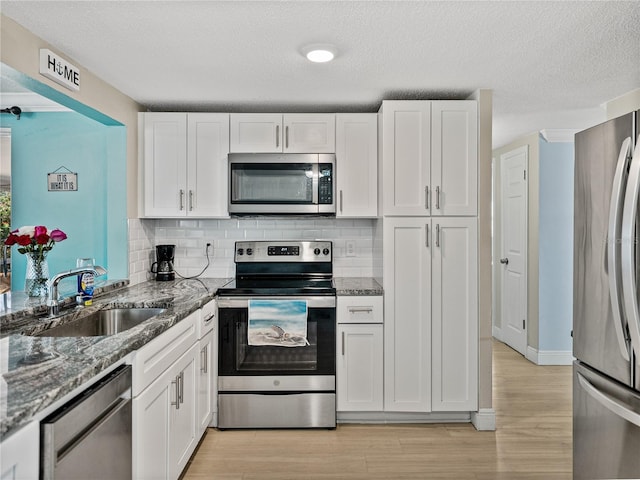 kitchen featuring stainless steel appliances, backsplash, stone countertops, white cabinets, and a sink