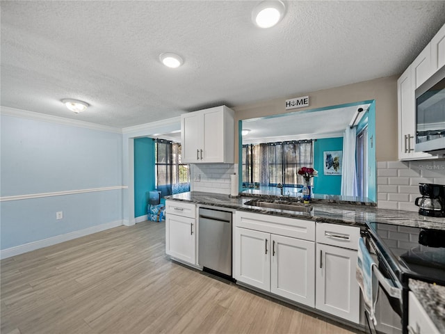 kitchen featuring stainless steel appliances, a sink, white cabinetry, light wood finished floors, and dark stone countertops