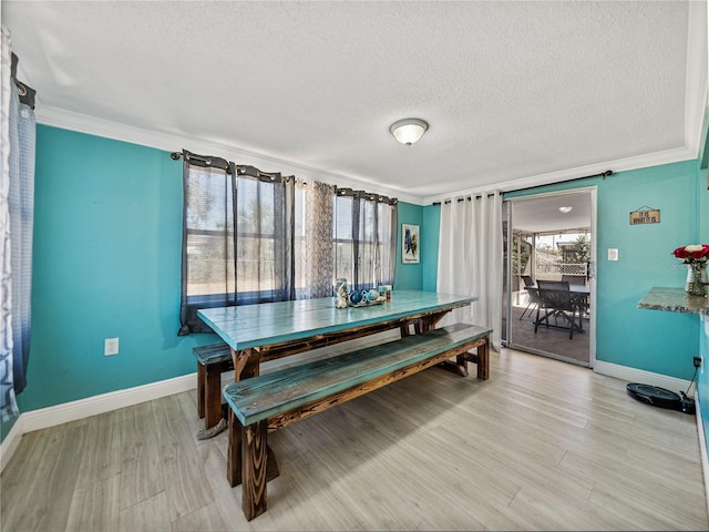 dining space featuring baseboards, crown molding, a textured ceiling, and light wood finished floors