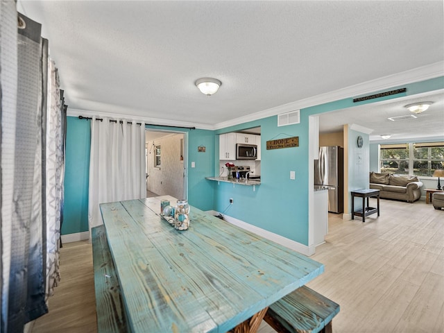 dining space featuring crown molding, visible vents, light wood-style flooring, a textured ceiling, and baseboards