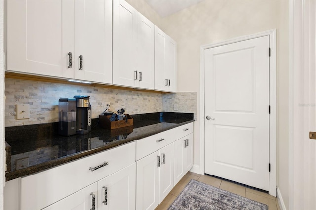 kitchen with light tile patterned floors, white cabinetry, backsplash, and dark stone countertops