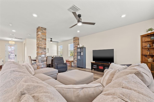 living area featuring ceiling fan, visible vents, decorative columns, and wood finished floors