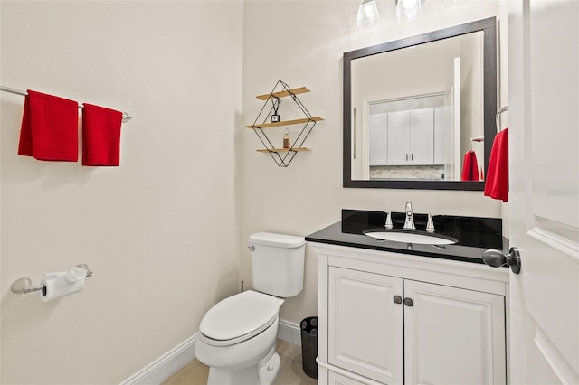 half bathroom featuring toilet, baseboards, and vanity