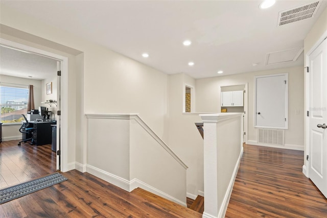 hallway featuring dark wood-style floors, recessed lighting, visible vents, and an upstairs landing