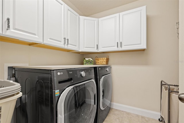 clothes washing area with light tile patterned flooring, independent washer and dryer, cabinet space, and baseboards