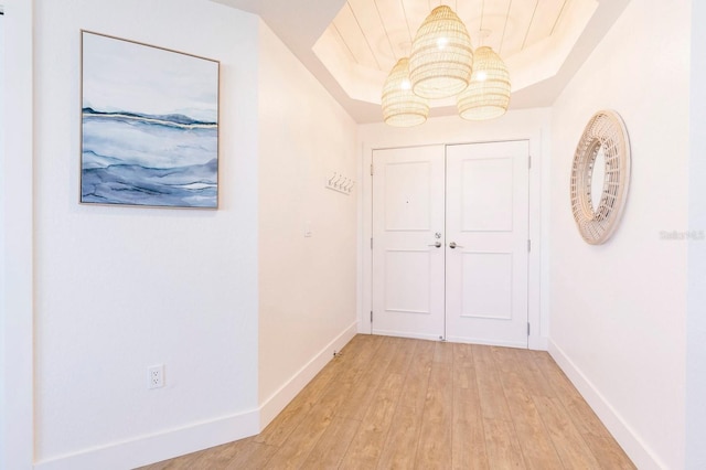 hall with a tray ceiling, light wood-style flooring, and baseboards