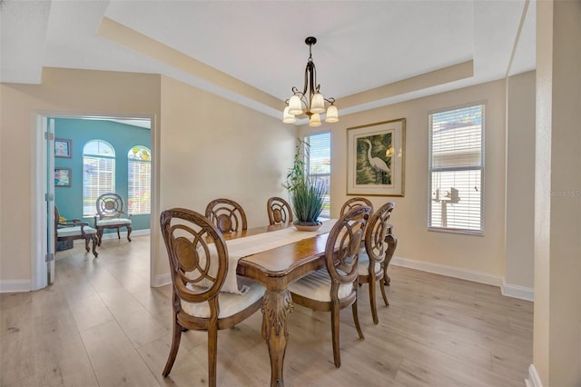 dining room with baseboards, a raised ceiling, an inviting chandelier, and light wood-style flooring