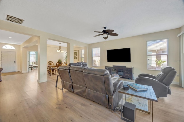 living room with visible vents, baseboards, light wood-style floors, and ceiling fan with notable chandelier