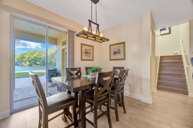 dining room with stairs, light wood-style flooring, baseboards, and a water view