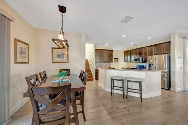 dining room with baseboards, visible vents, light wood finished floors, recessed lighting, and stairs