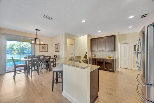 kitchen with visible vents, dark brown cabinets, freestanding refrigerator, and a sink