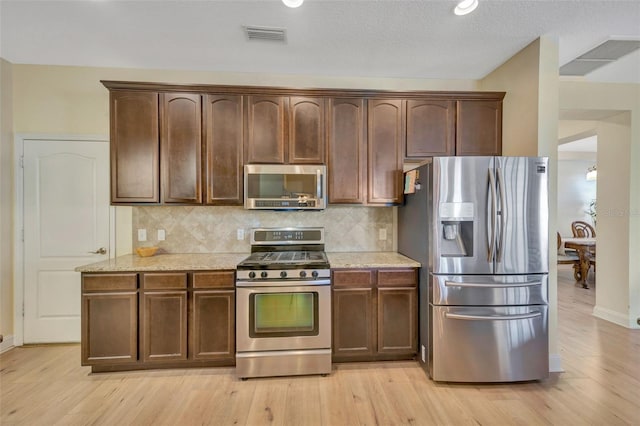 kitchen featuring visible vents, light wood-style flooring, appliances with stainless steel finishes, decorative backsplash, and light stone countertops